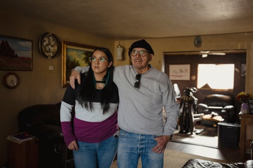 A man wearing a black hat and glasses stands with his arm around a woman with long, dark hair and wearing glasses