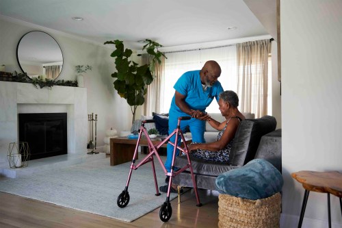 A photo of a home health aide helping an older woman sit down.