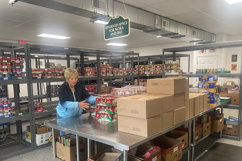 A woman standing before a metal table sorts boxes of non-perishable foods