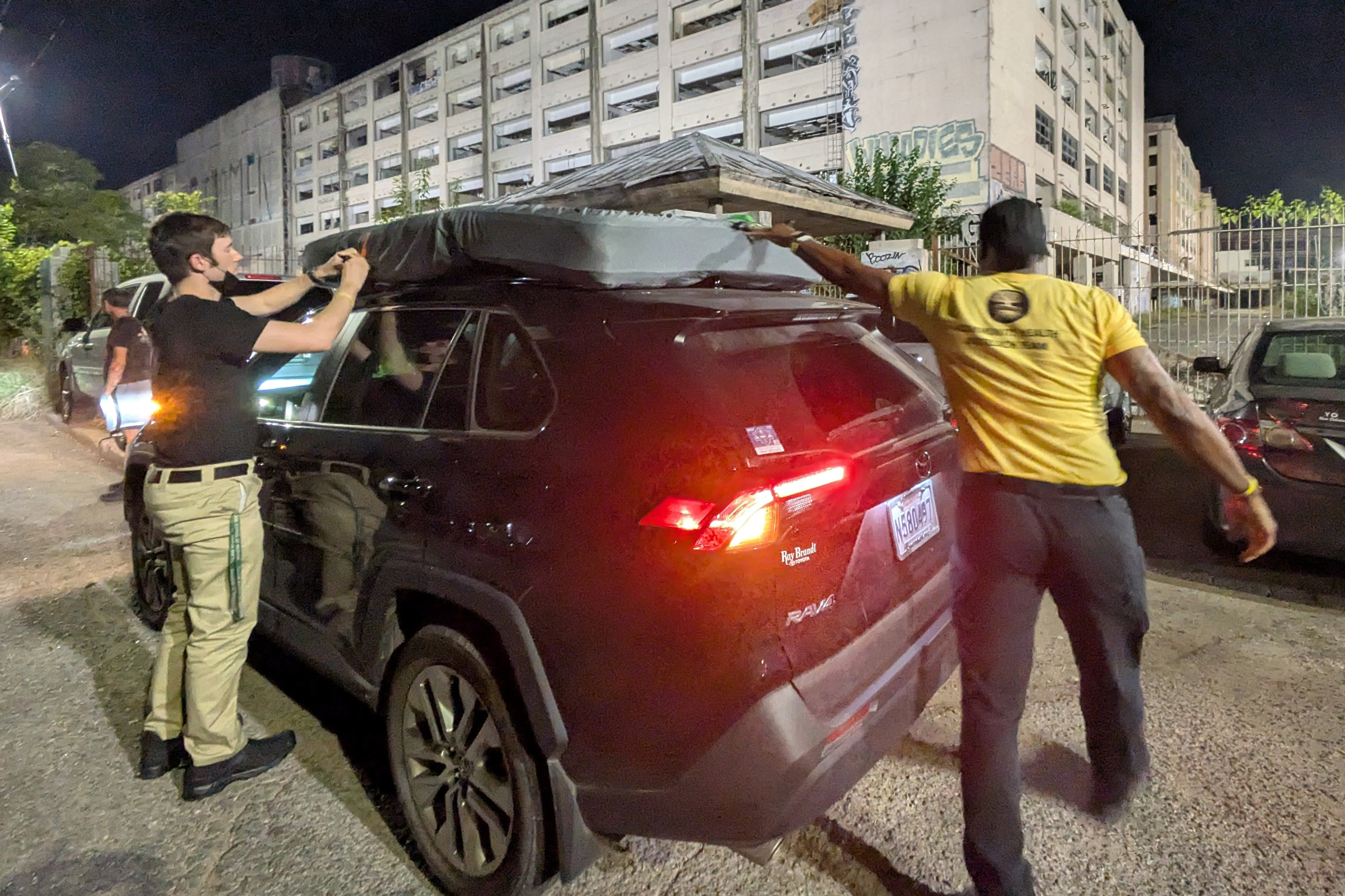 A photo of pople loading a mattress on top of an SUV.