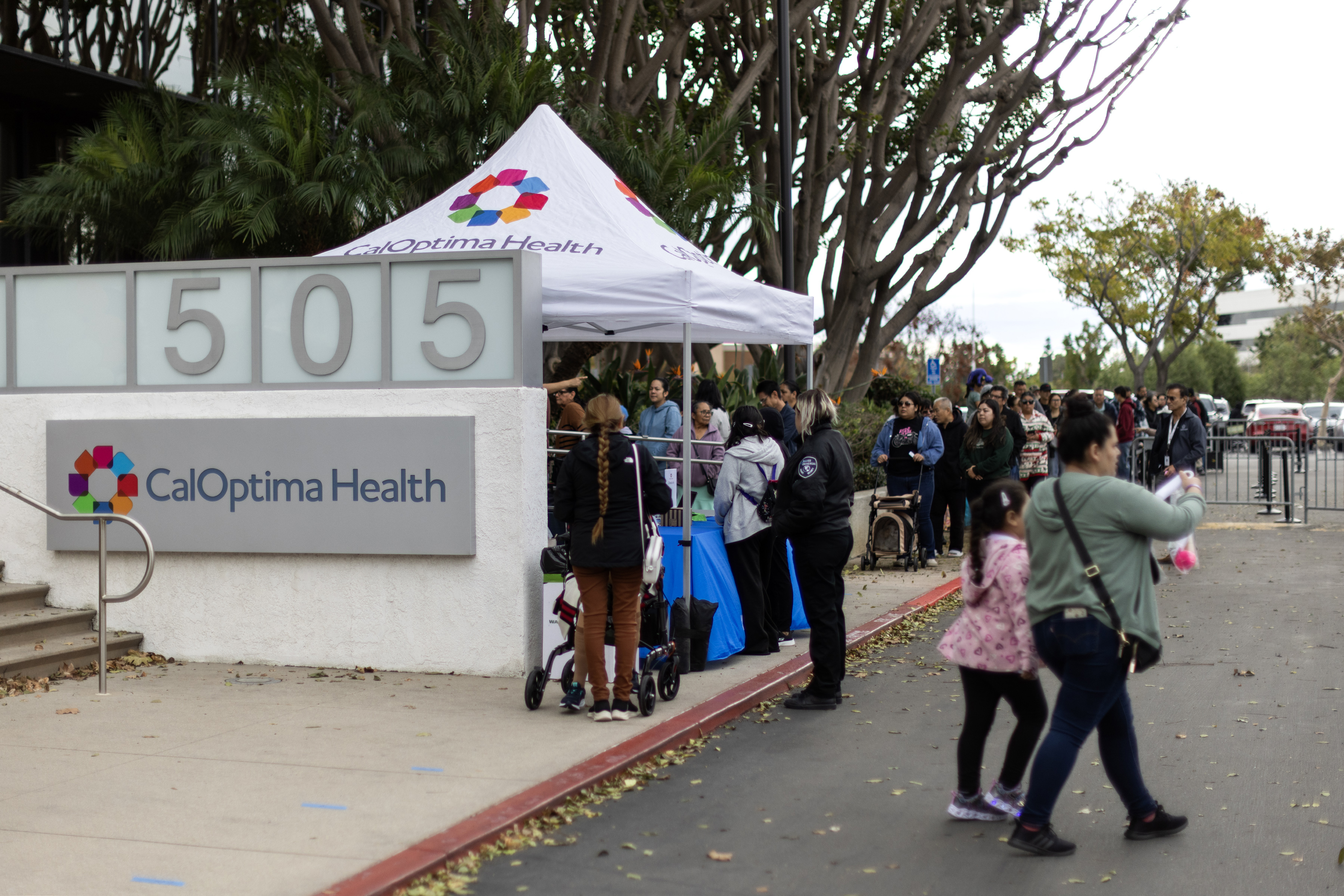 A photo of a line of people at a tent with the CalOptima logo on it.