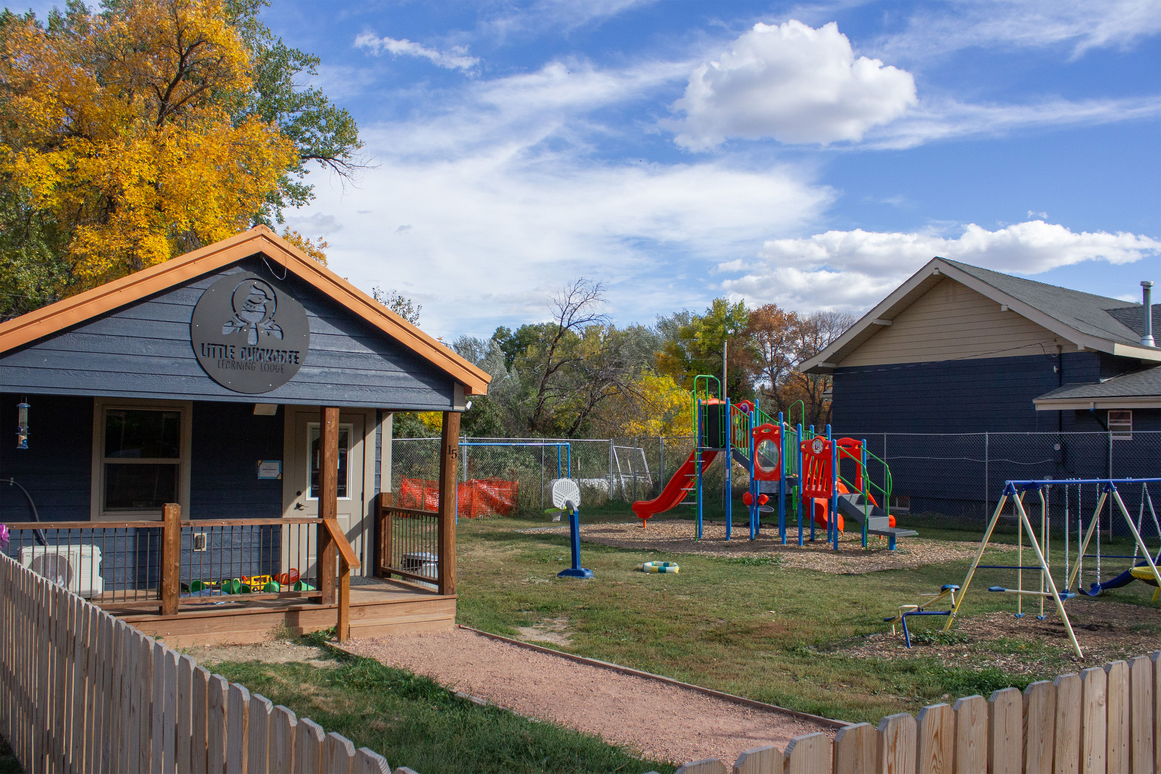 A fenced-in playground also has a small building with a sign above the entrance reading "Little Chickadee Learning Lodge."