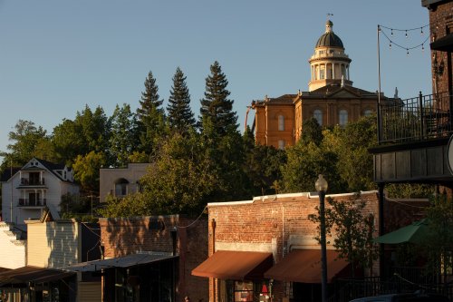 A photo of a historic downtown area of Auburn, California. Old buildings are seen alongside trees. A rotunda is seen on top of a tall building in the background.