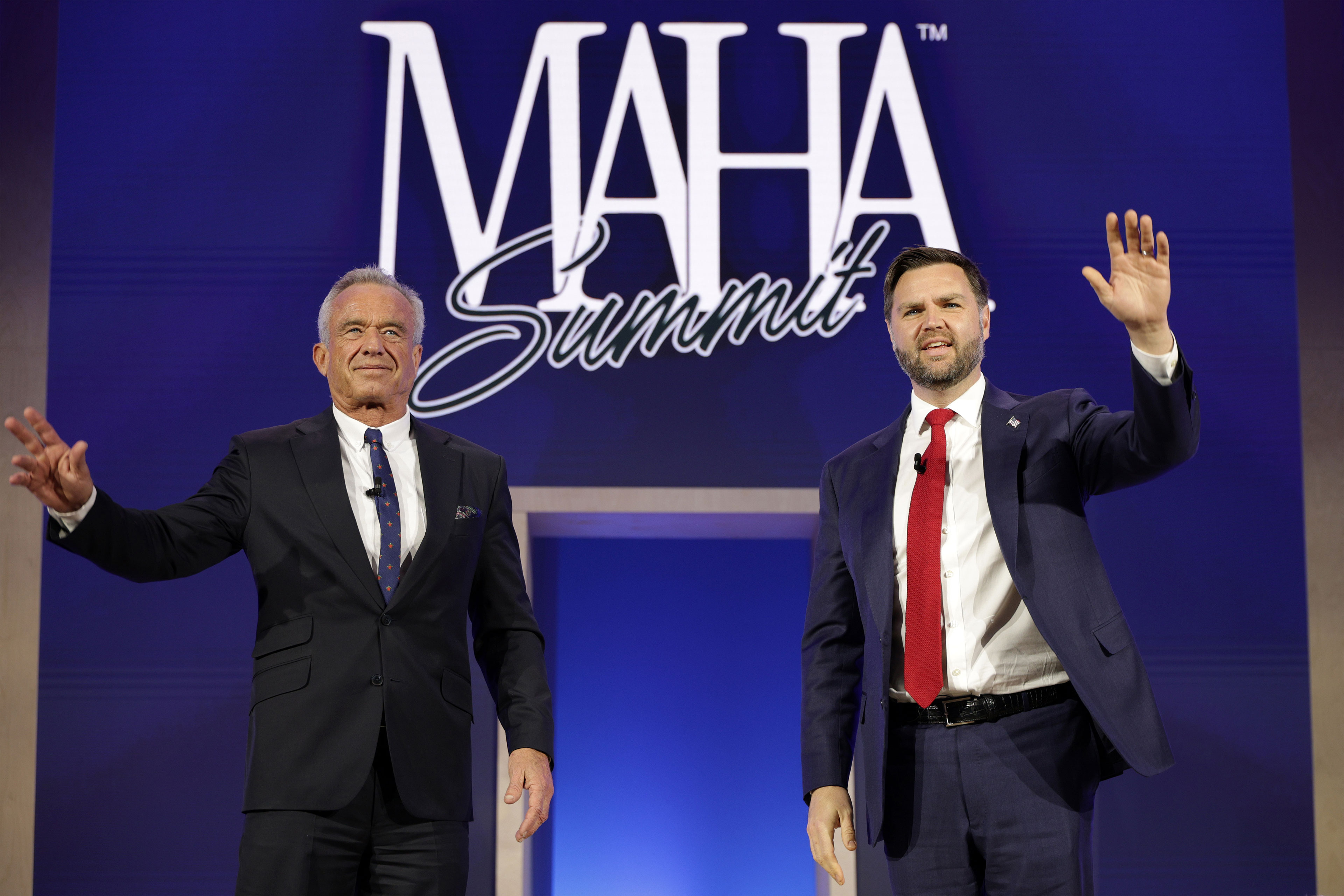 A photo of Robert F. Kennedy Jr. and JD Vance waving to an audience at a conference in D.C. Behind them is a sign reading "MAHA Summit."