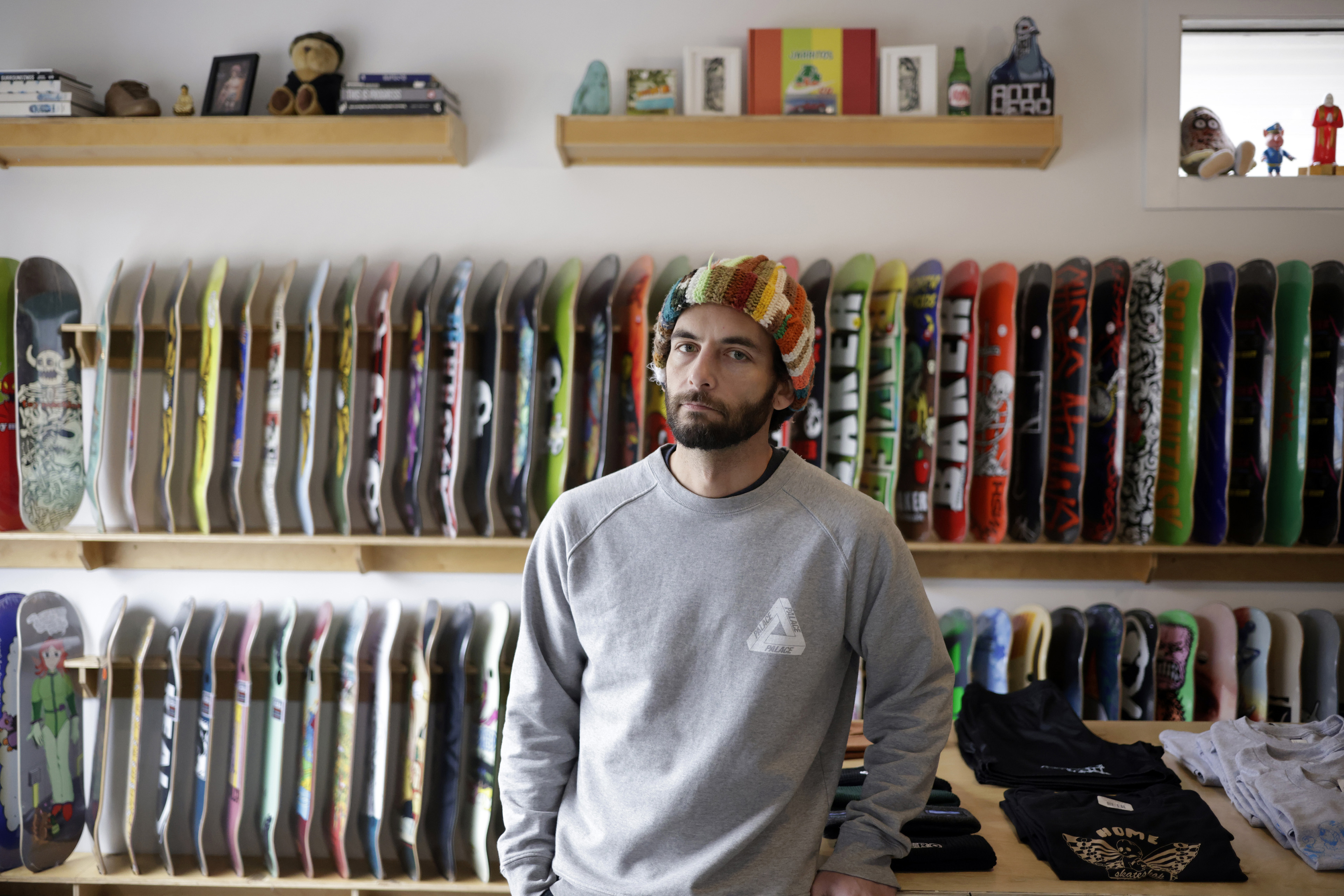 A man wearing a multicolor hat stands in front of two shelves of skateboards