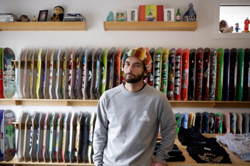 A man wearing a multicolor hat stands in front of two shelves of skateboards