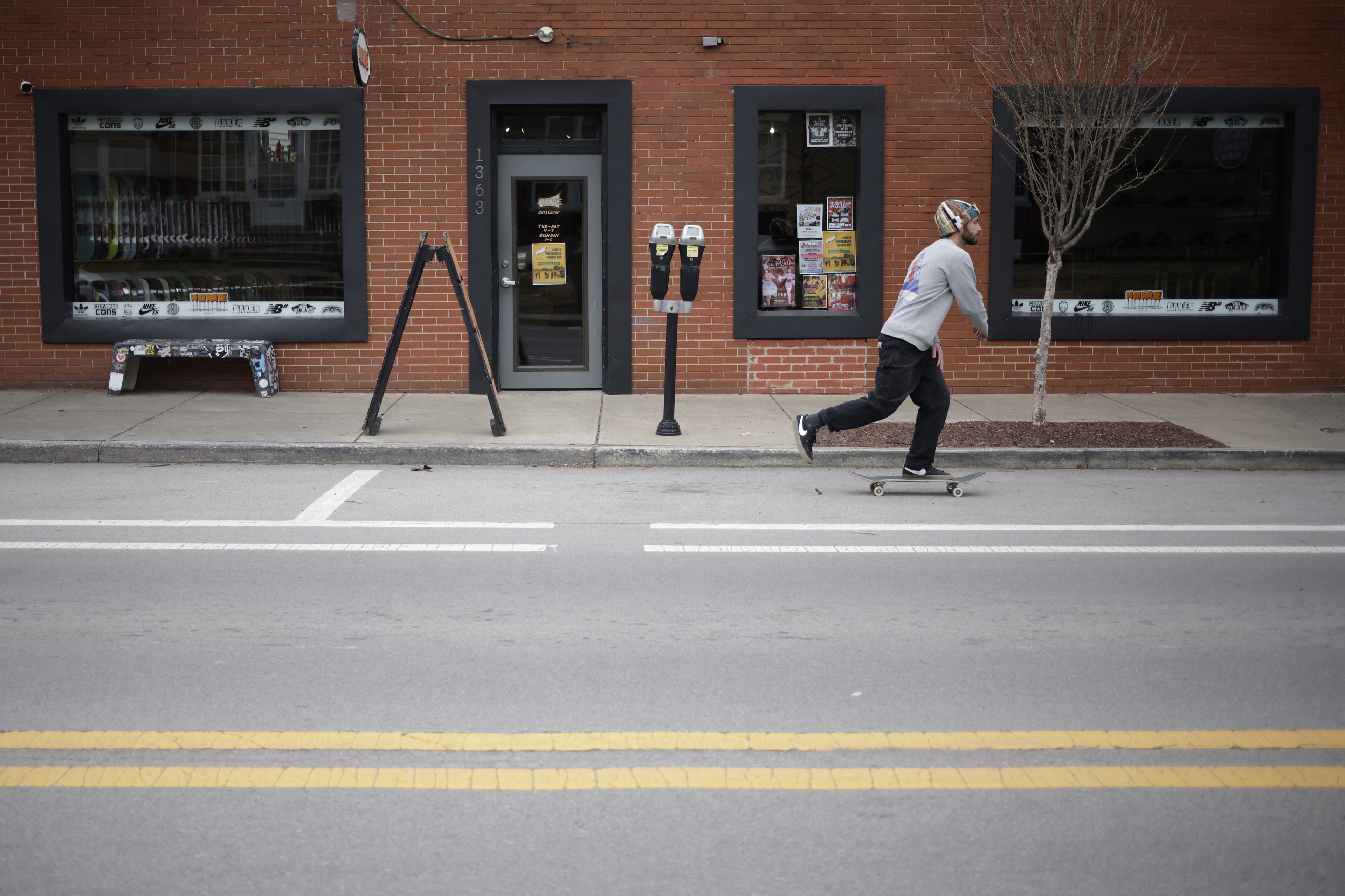 A man skateboards on the side of the street in front of a brick building