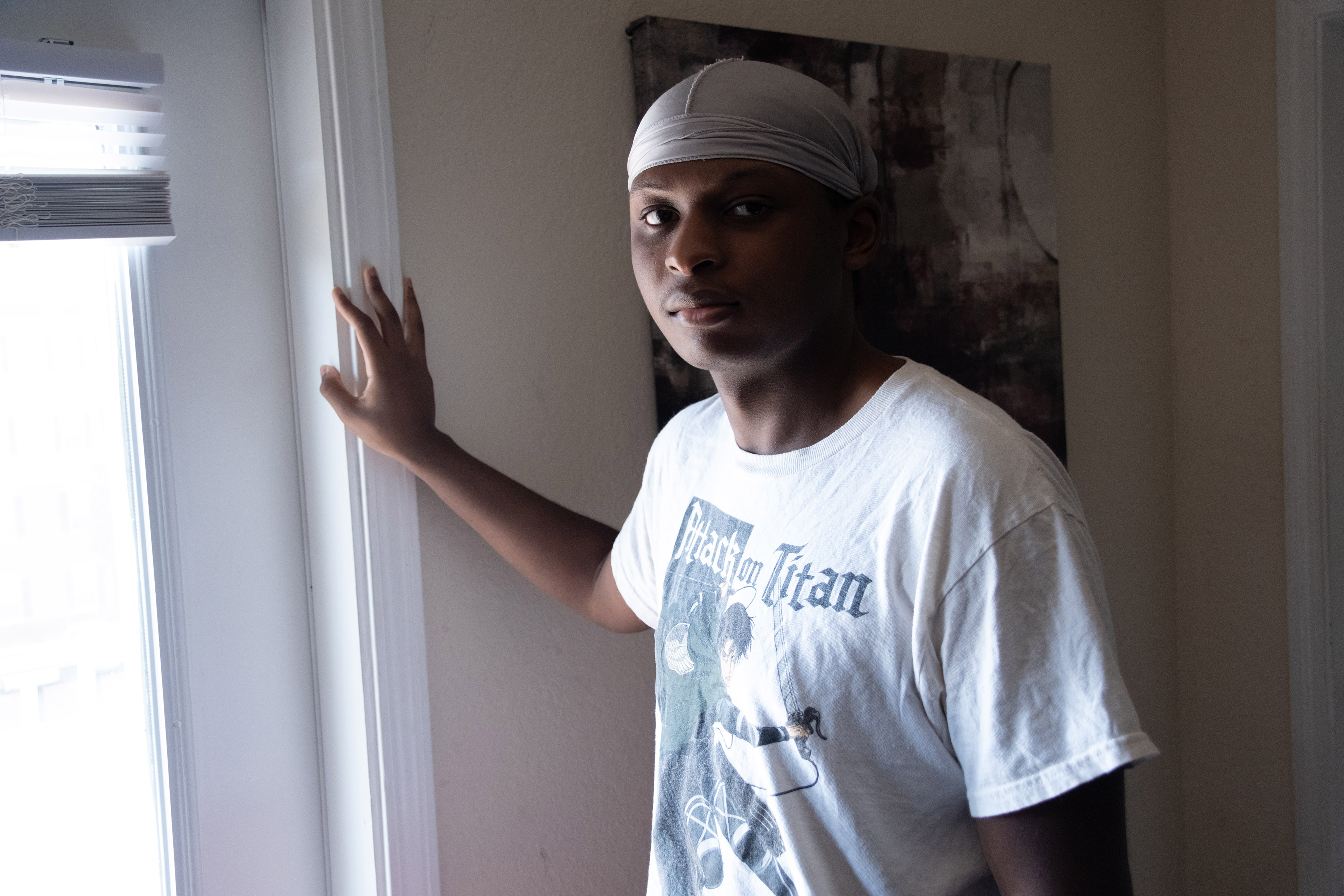 A man wearing a white t-shirt poses for a photo in front of a window