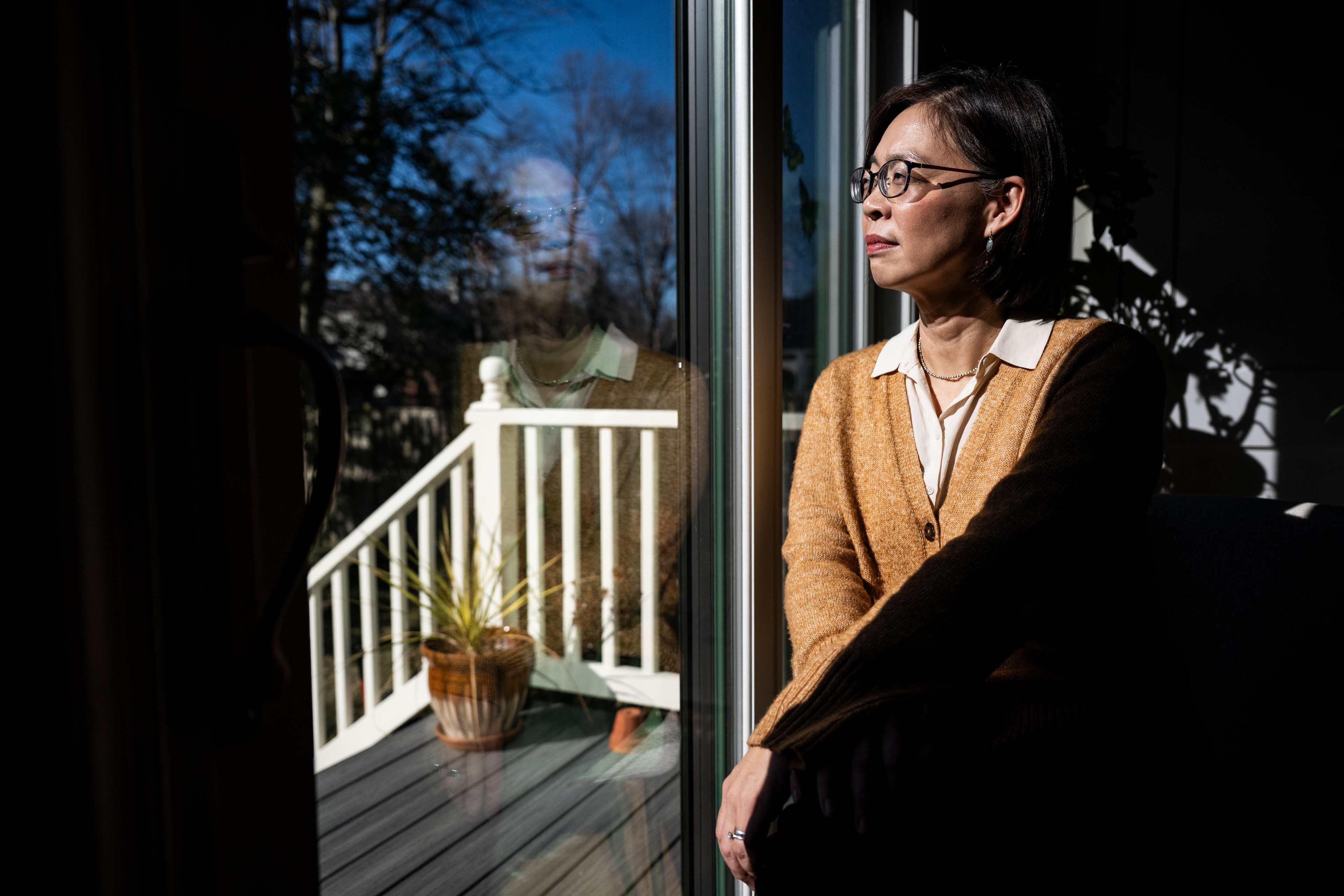A woman in a yellow cardigan sits in front of a window, staring out