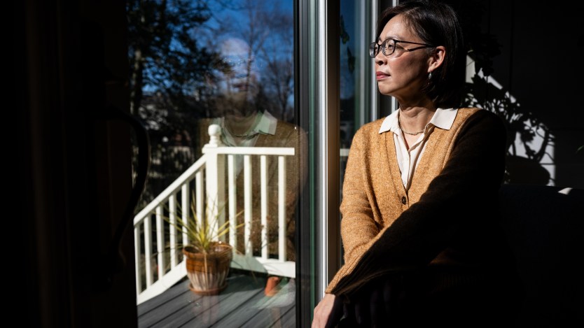 A woman in a yellow cardigan sits in front of a window, staring out