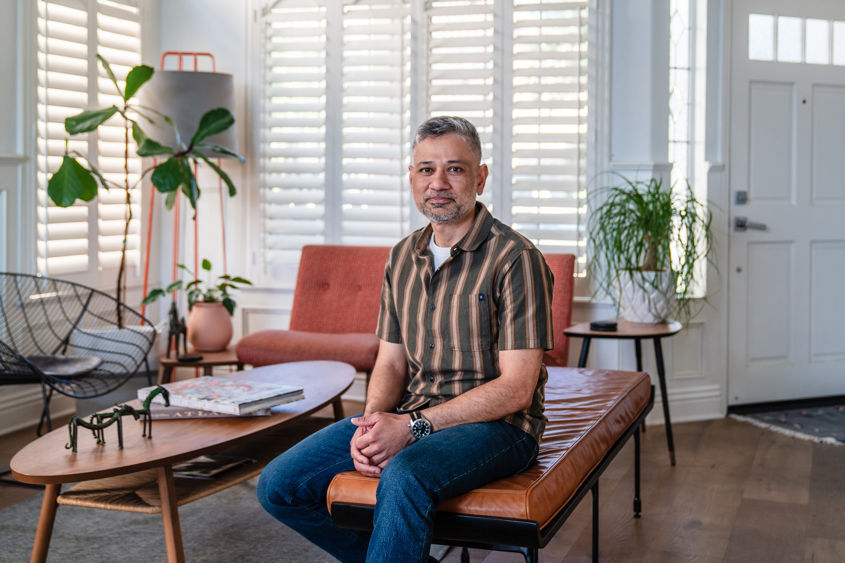 Jayant Mishra sits in his living room. Two leafy plants are in pots behind him.