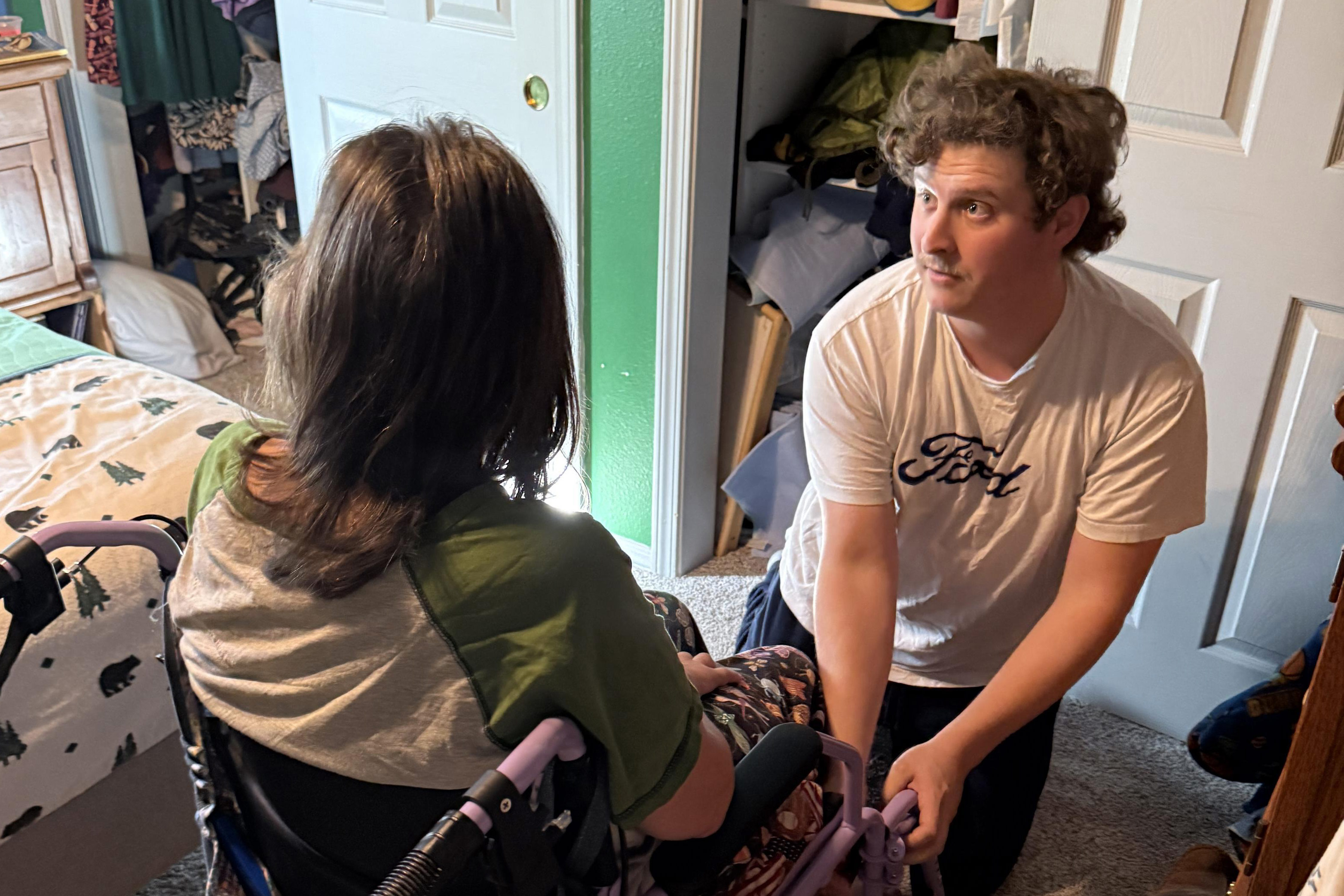 A photo of Charlie Franklin assisting Jean Franklin get out of her wheelchair.