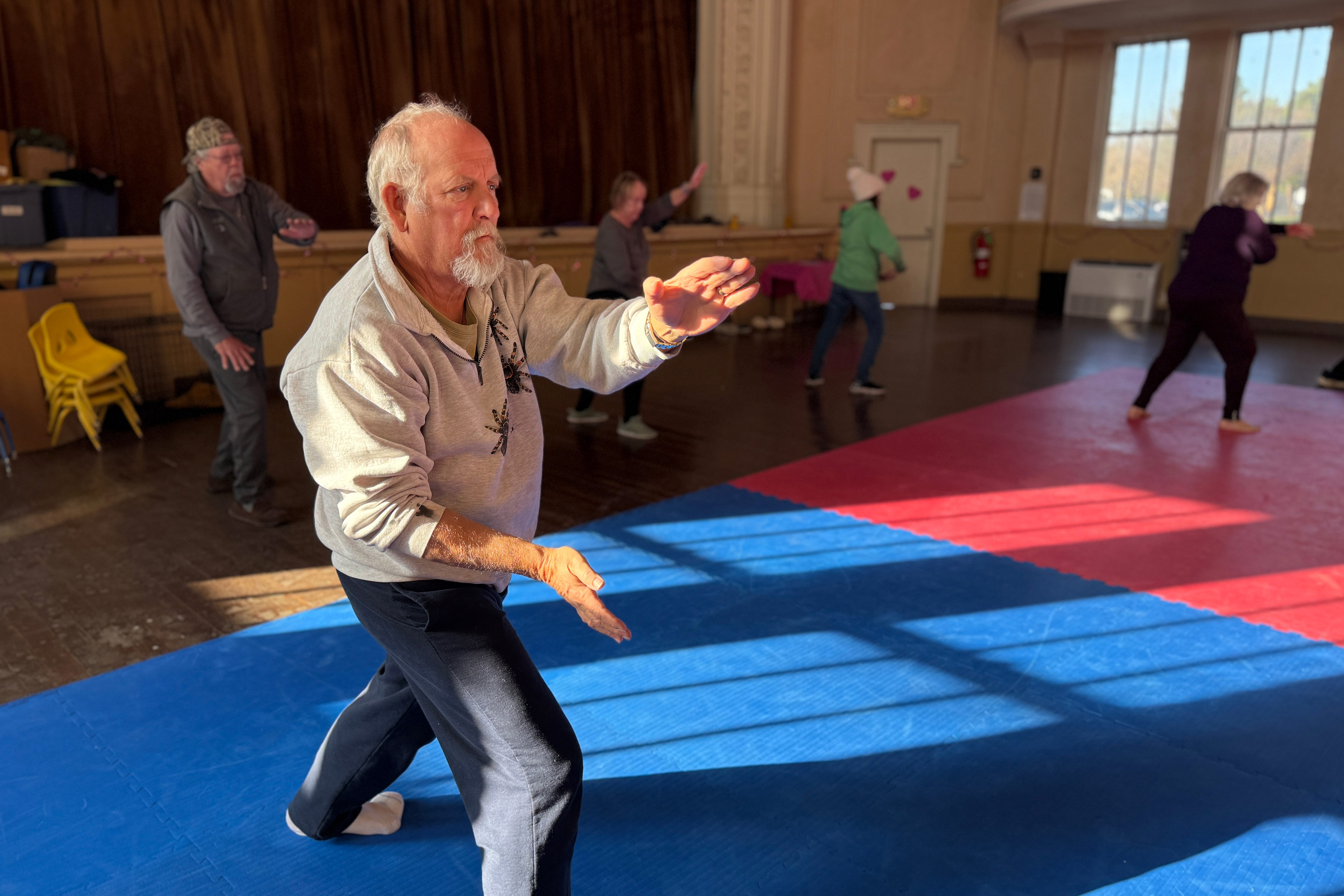 Chaz Franklin is seen practicing tai chi at a class in an auditorium.