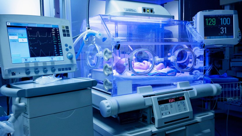 A baby lies in an incubator in a neonatal intensive care unit.