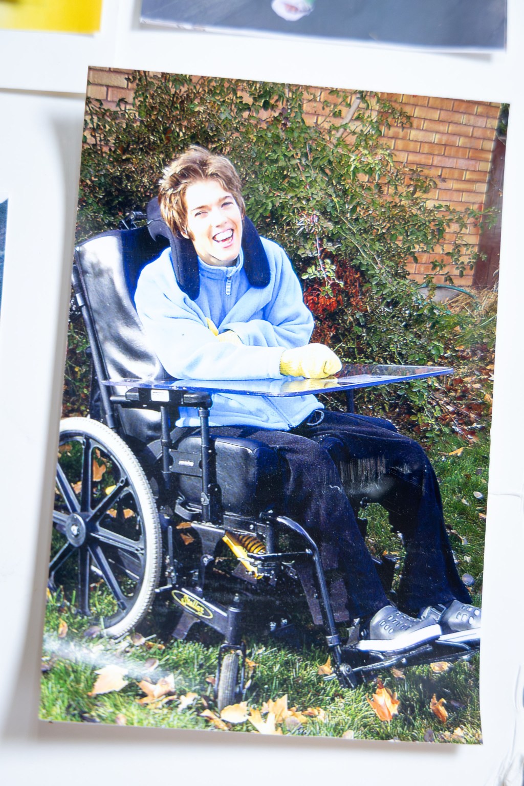 A photograph of a printed picture of a woman smiling as she sits in a wheelchair outdoors