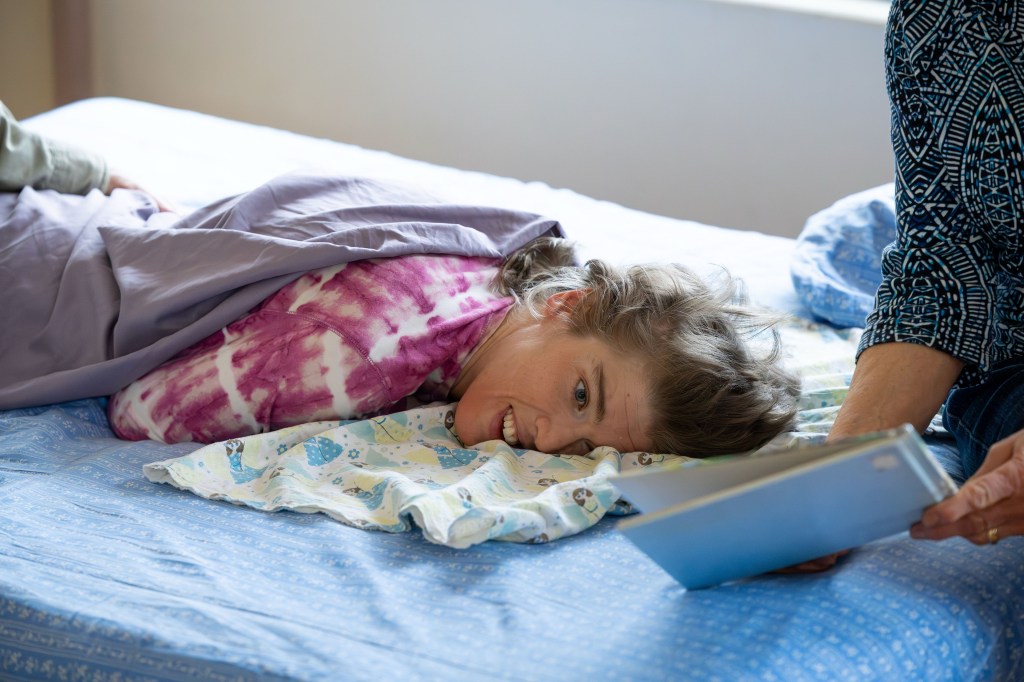 A woman lies on a bed as a book is held in front of her
