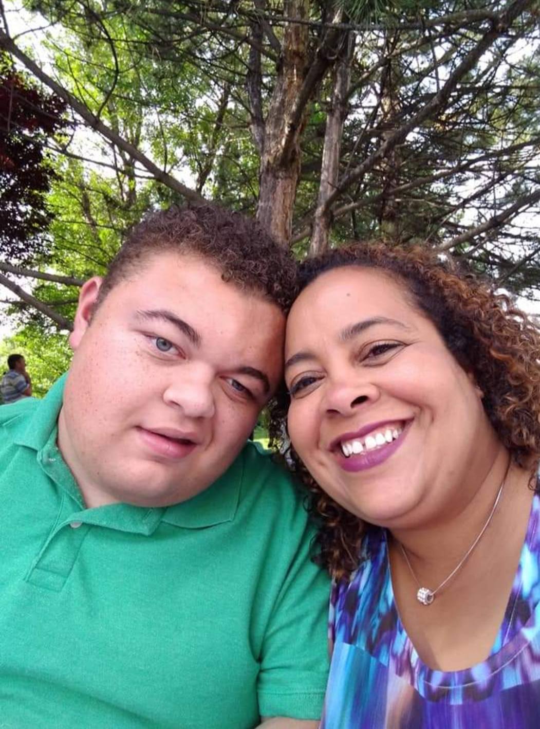 A man in a green collared shirt sits next to a woman with brown curly hair as they both smile for a selfie