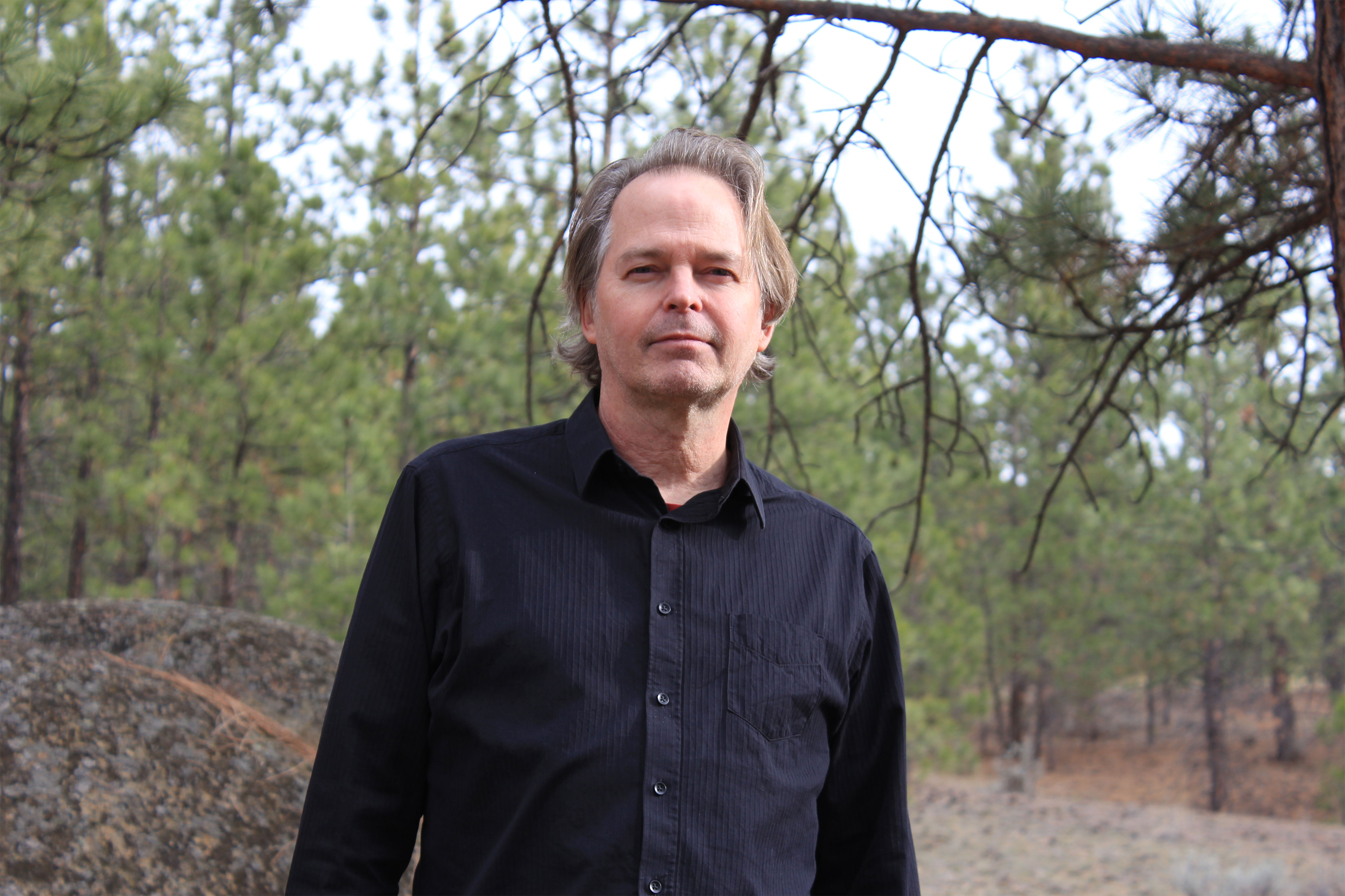 A man stands outside in a wooded area.