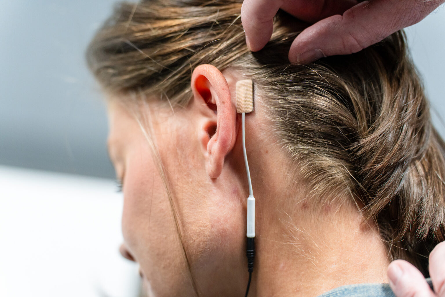 A small gel electrode with a cord is seen placed behind a woman's ear.