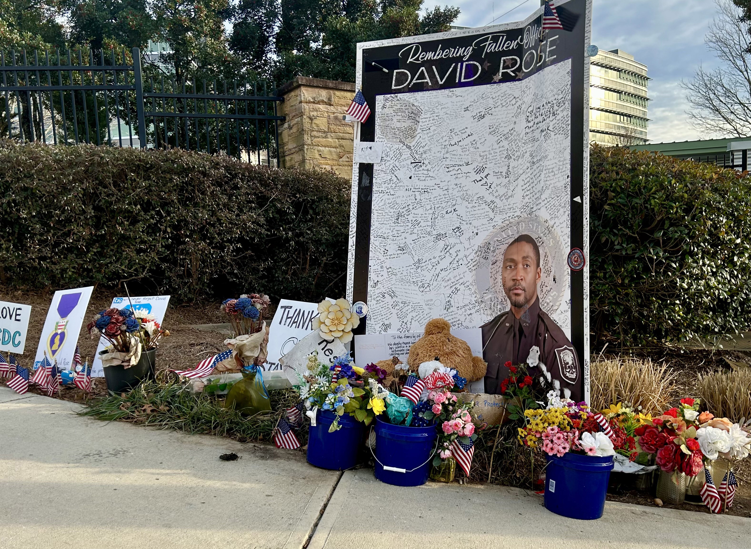 Flowers and flags surround a memorial for DeKalb County police officer David Rose next to a sidewalk