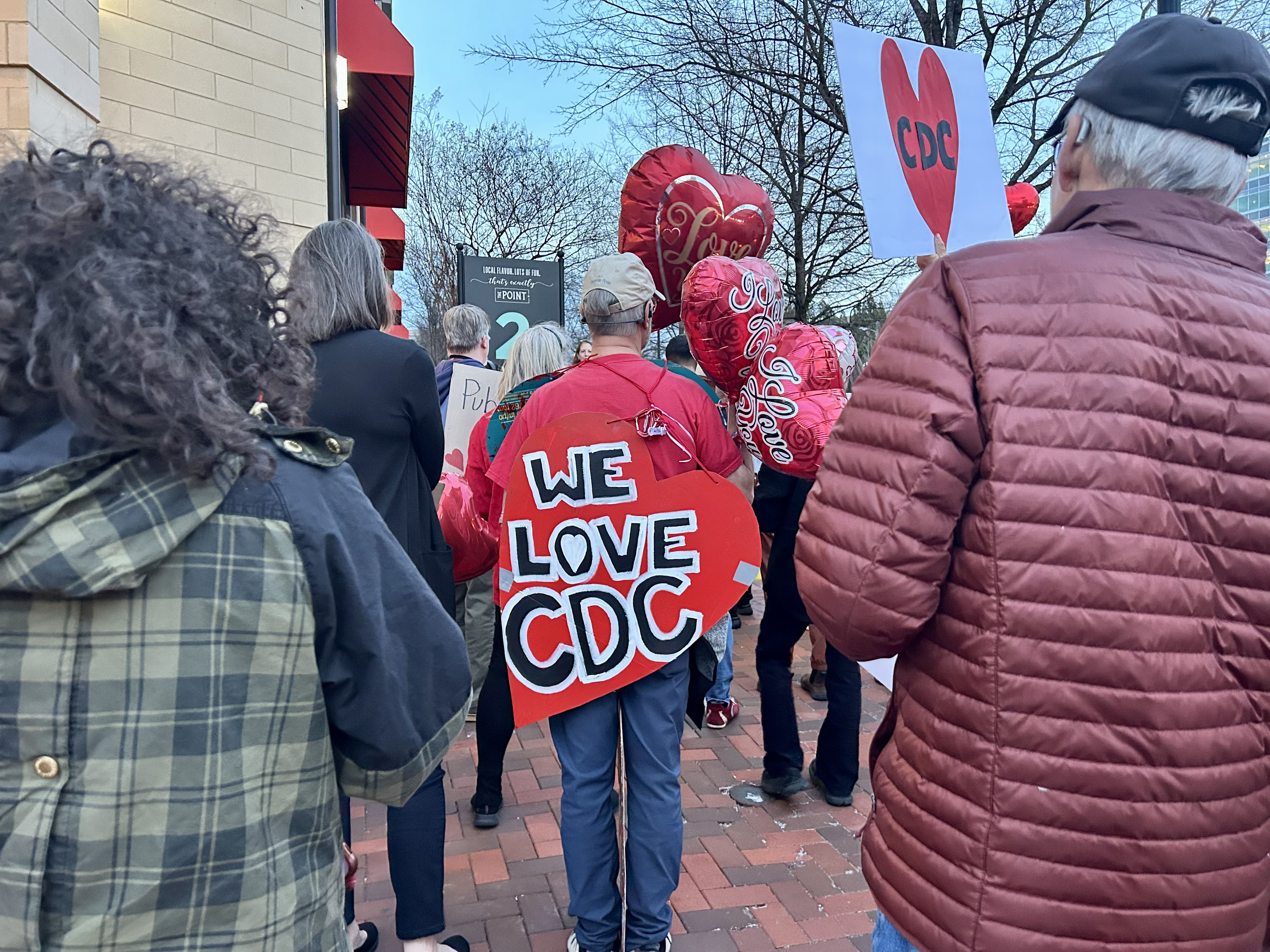 Protestors stand with love balloons and a heart sign that reads "We love CDC"