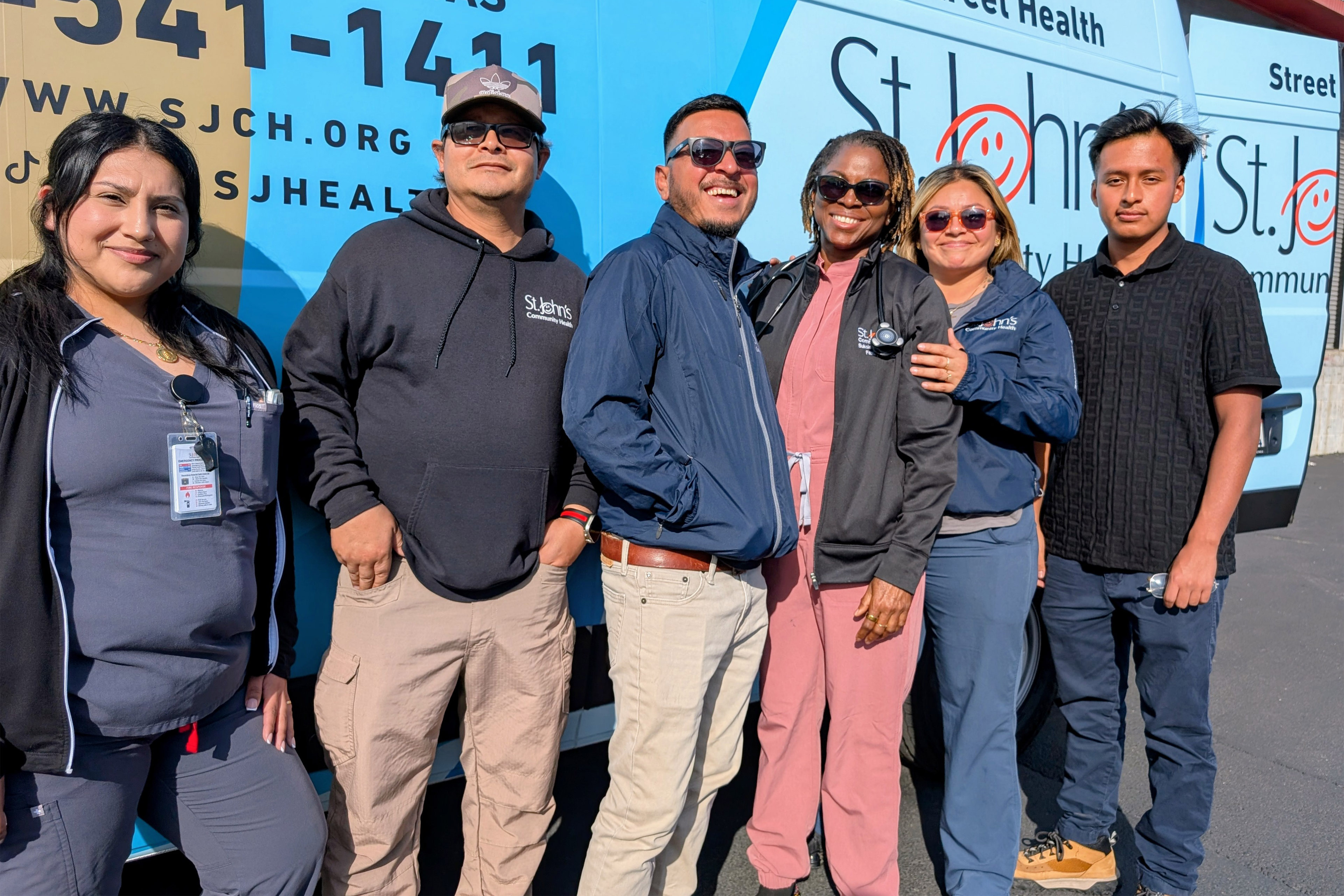A row of five people stand in front of a van they use for street medicine services.
