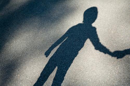 A shadow of a young boy is cast against the pavement. The boy is holding an adult's hand out of frame.