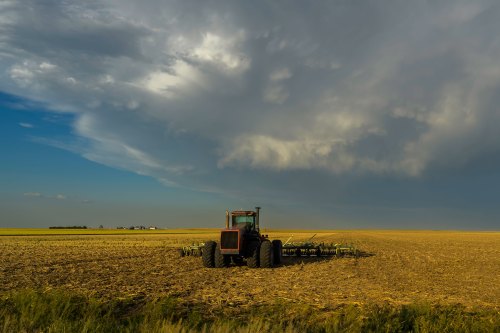 A tractor is parked in a field. Dark clouds are moving overhead.