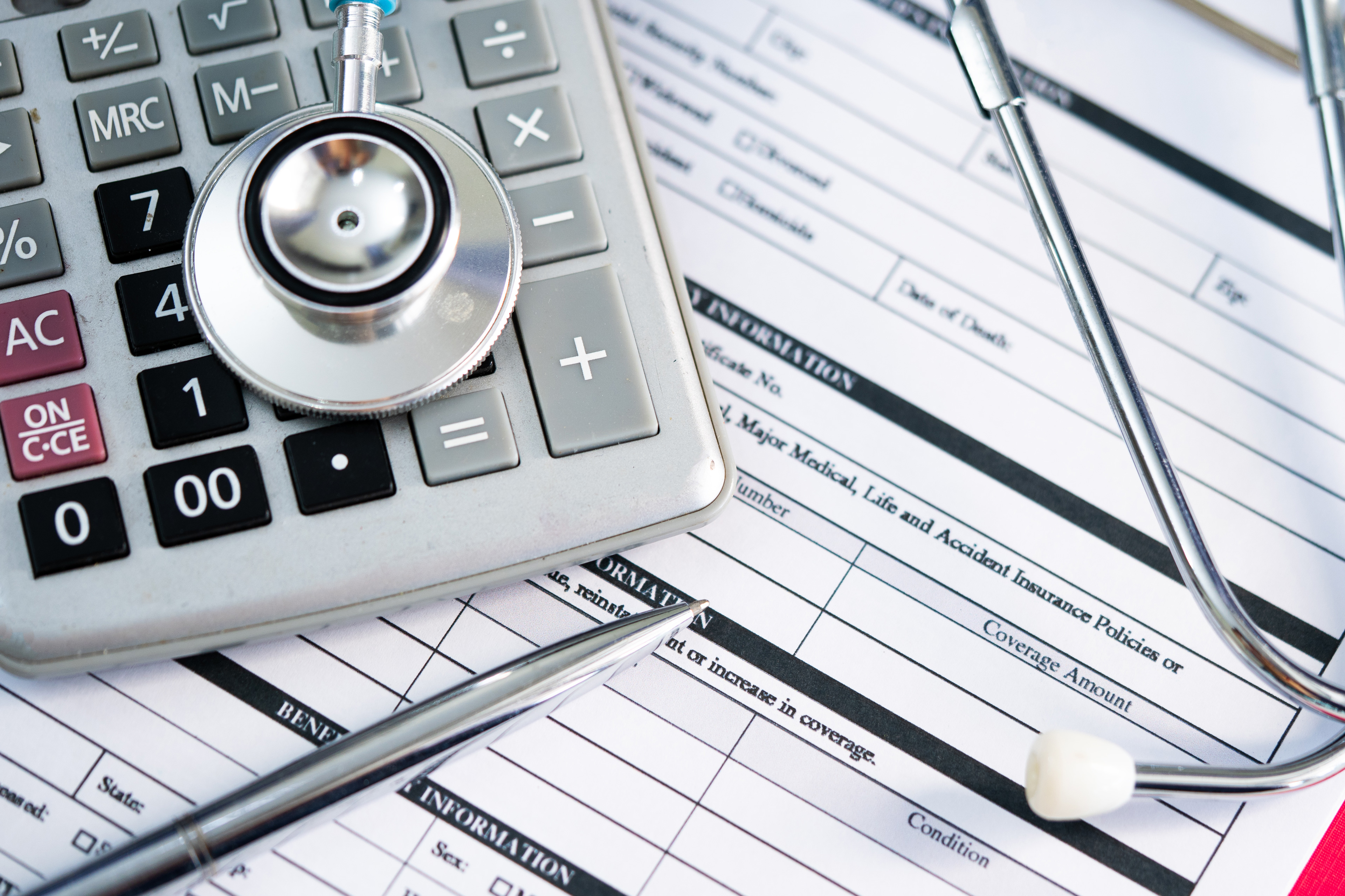 A photo of health insurance paperwork with a stethoscope and calculator resting on top.