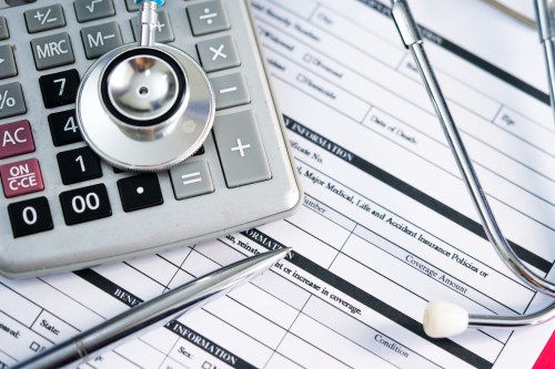 A photo of health insurance paperwork with a stethoscope and calculator resting on top.