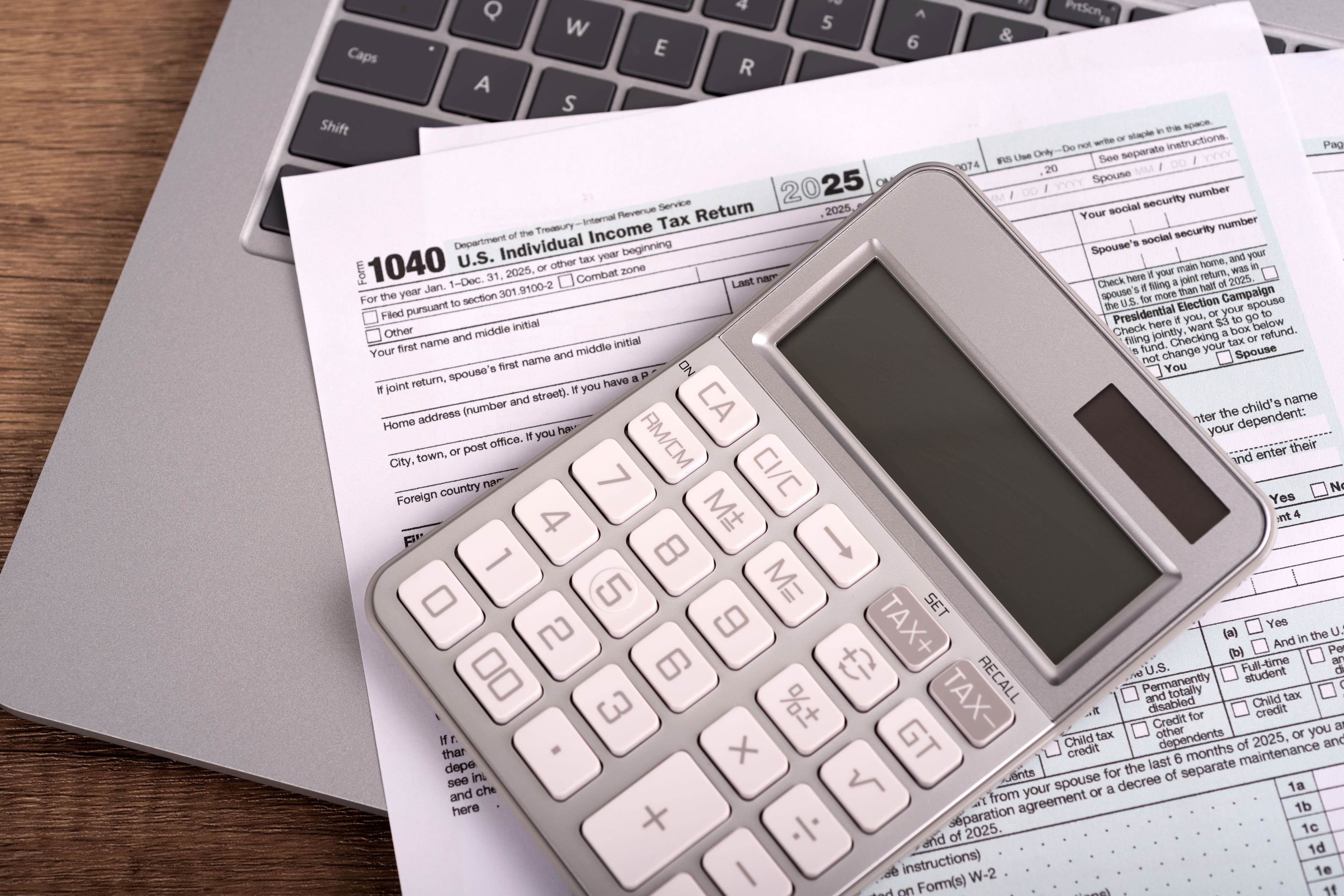 A set of tax forms and a calculator rest on top of a laptop.