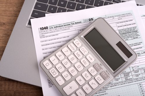 A set of tax forms and a calculator rest on top of a laptop.