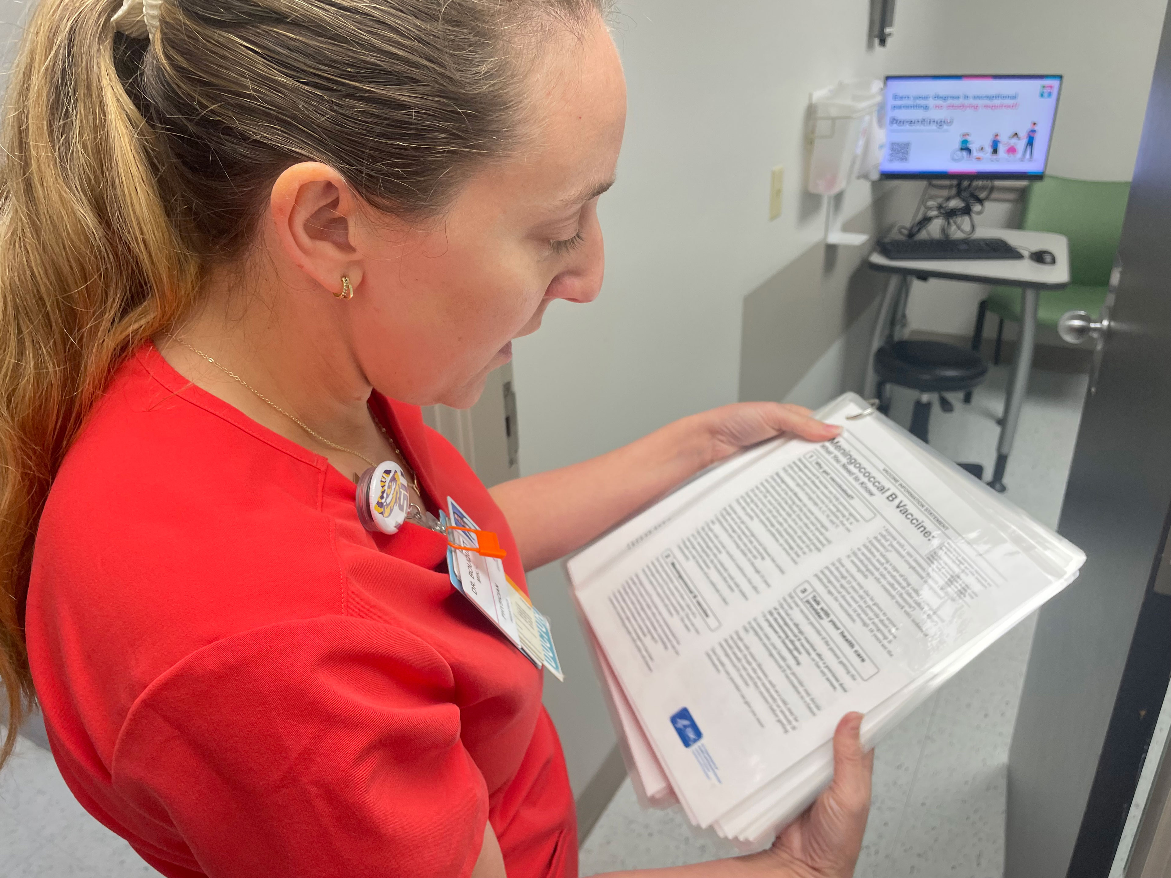 A photo of Mikki Bouquet reads a laminated page about the Meningococcal B vaccine.