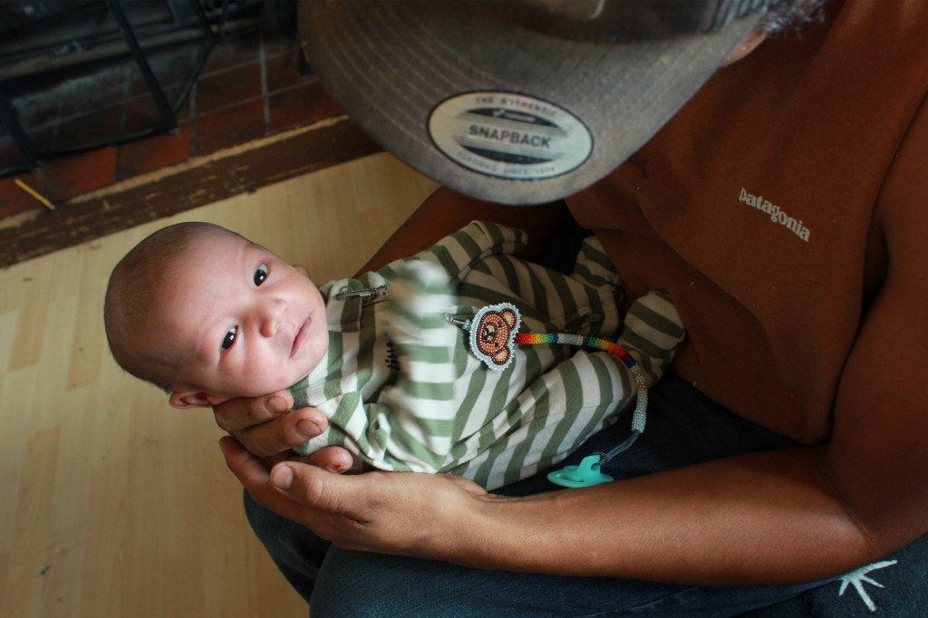 A father holds a baby in striped green pajamas in his arms.