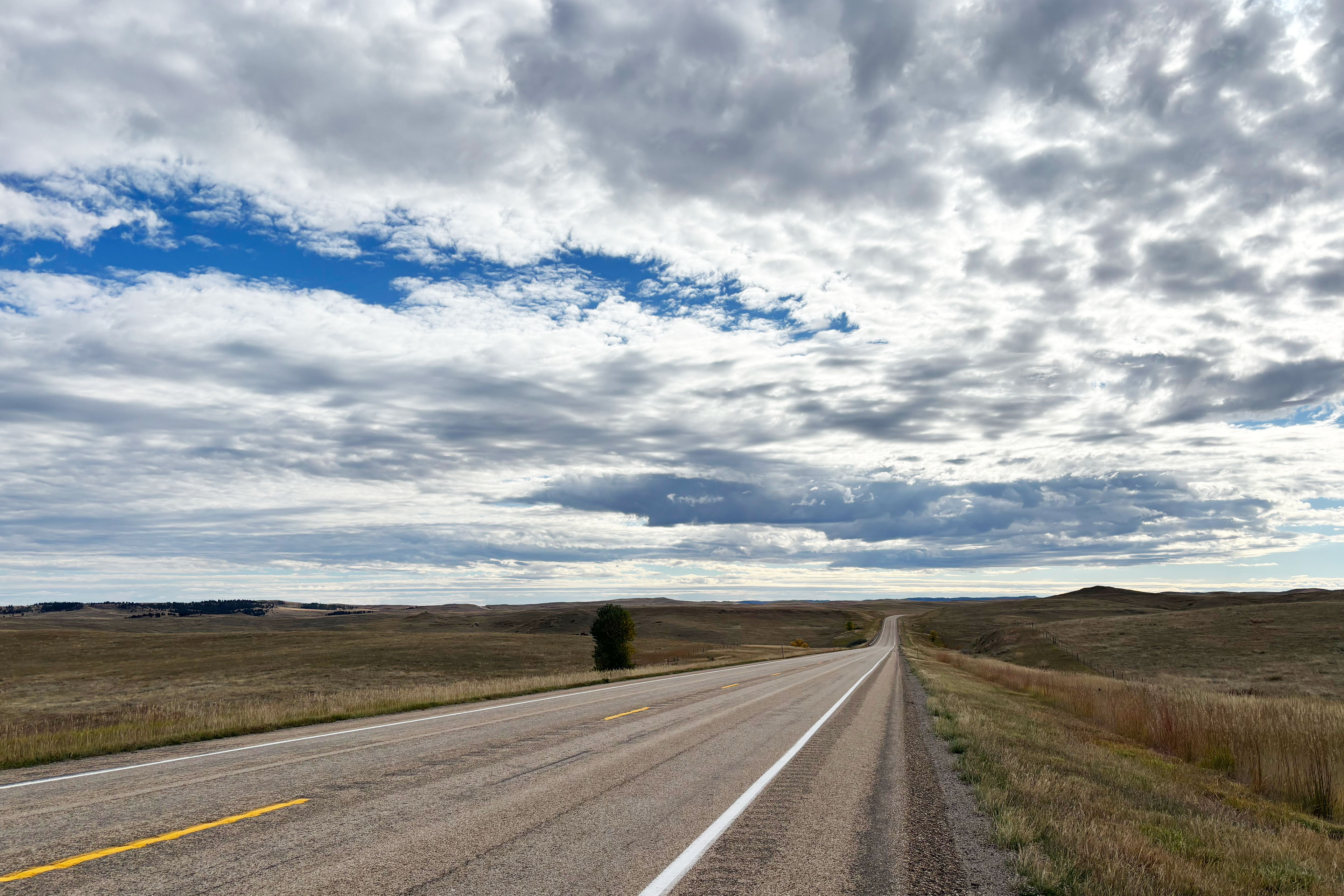 A landscape shot of a road in rural Montana. The sky above it is filled with clouds.