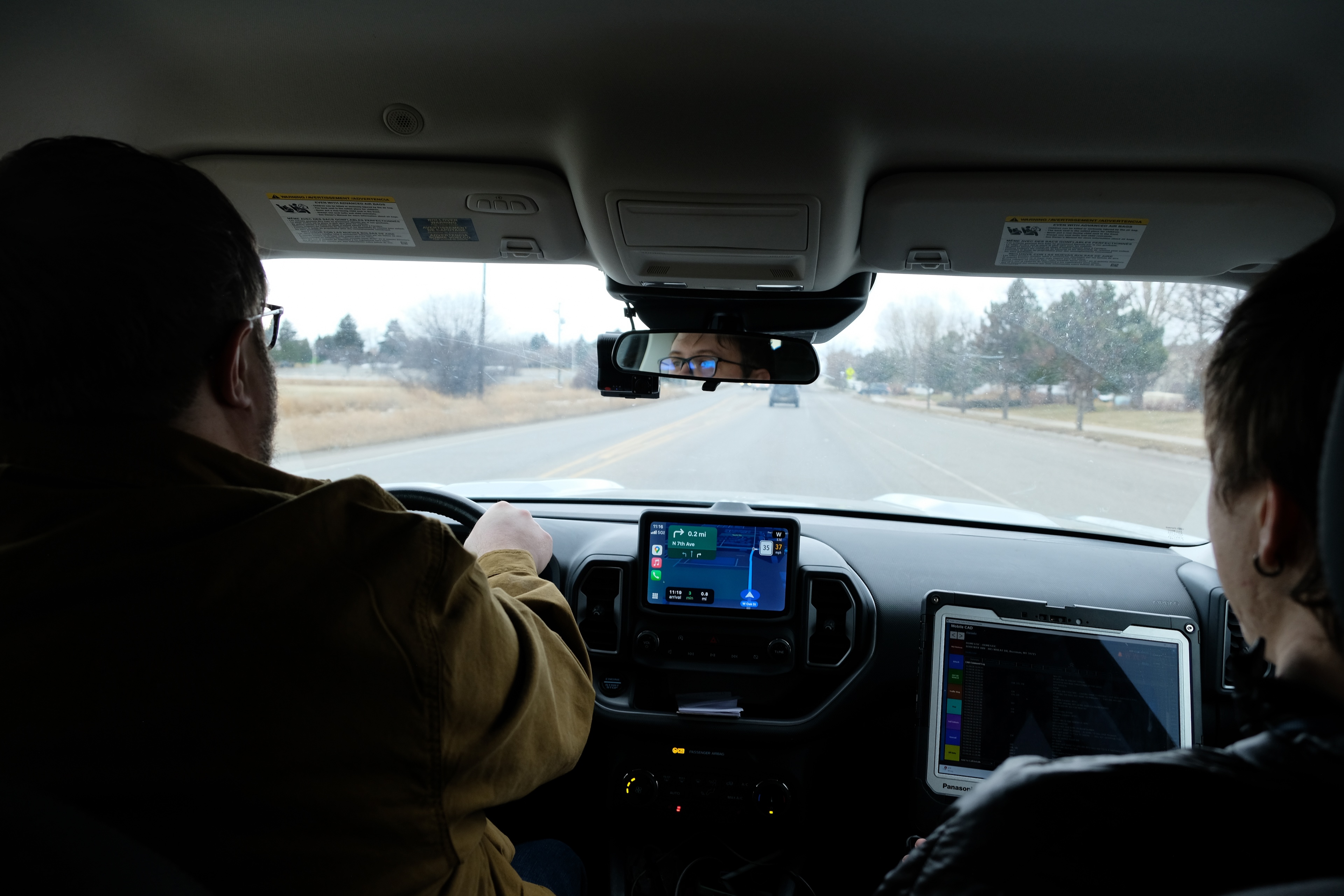 A photo from the back seat of a car, two men in the front and passenger seat driving