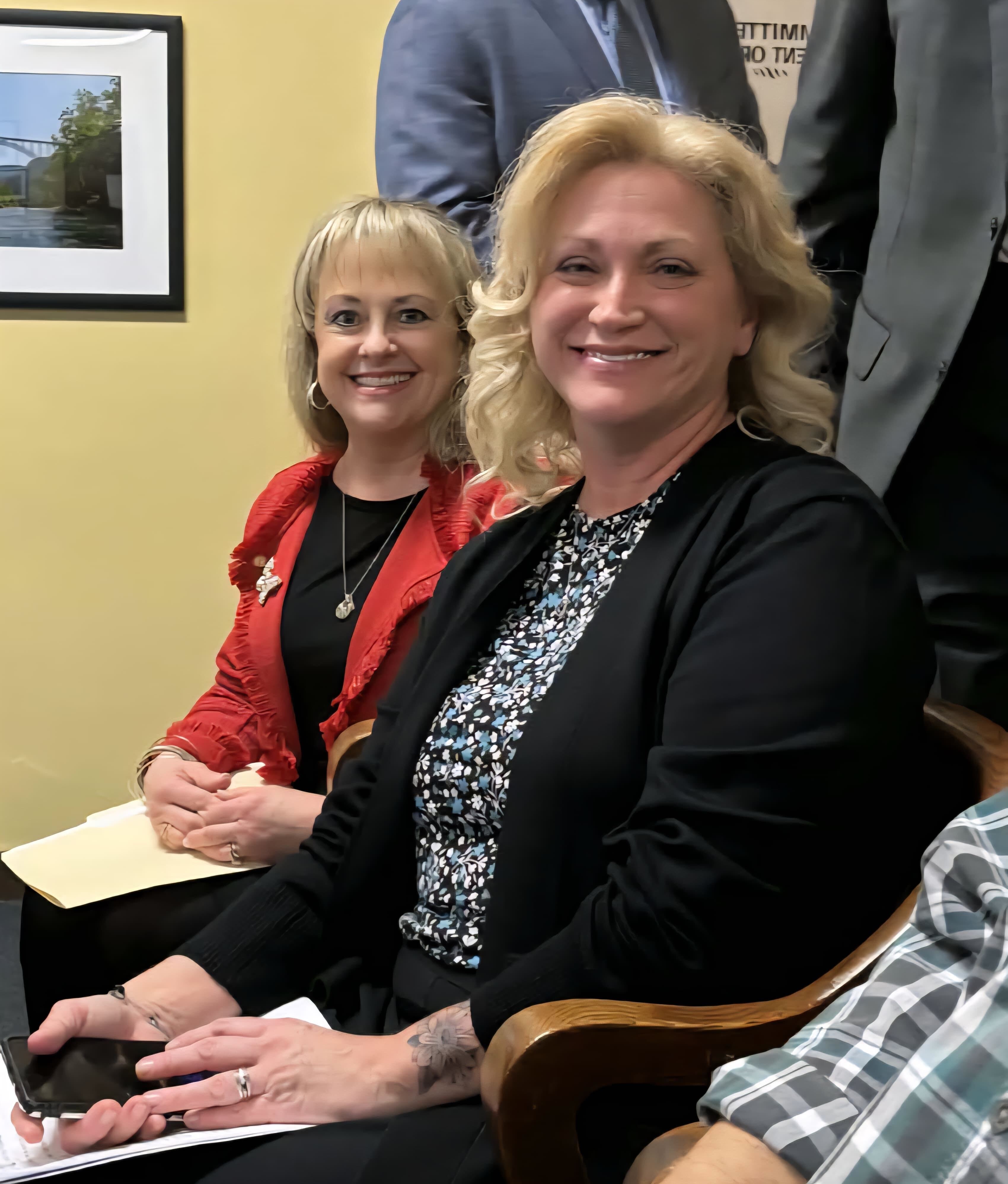 Laura Kimble and Becky Tennant smile for a photo while seated at a hearing of the West Virginia House of Representatives.