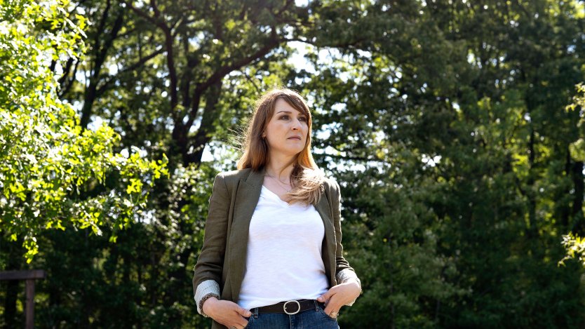 A woman stands outside in a park surrounded by trees.
