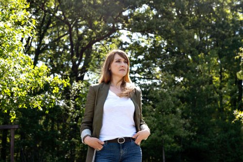 A woman stands outside in a park surrounded by trees.