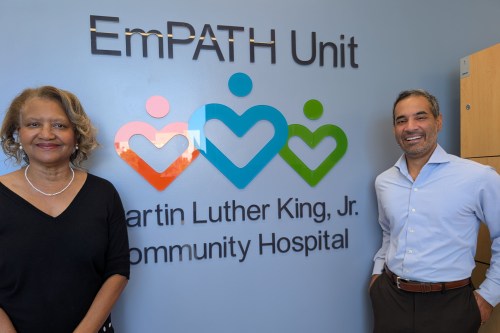 A woman and a man in business formal attired stand on either side of a sign that says, "EmPATH Unit / Martin Luther King Jr. Community Hospital."