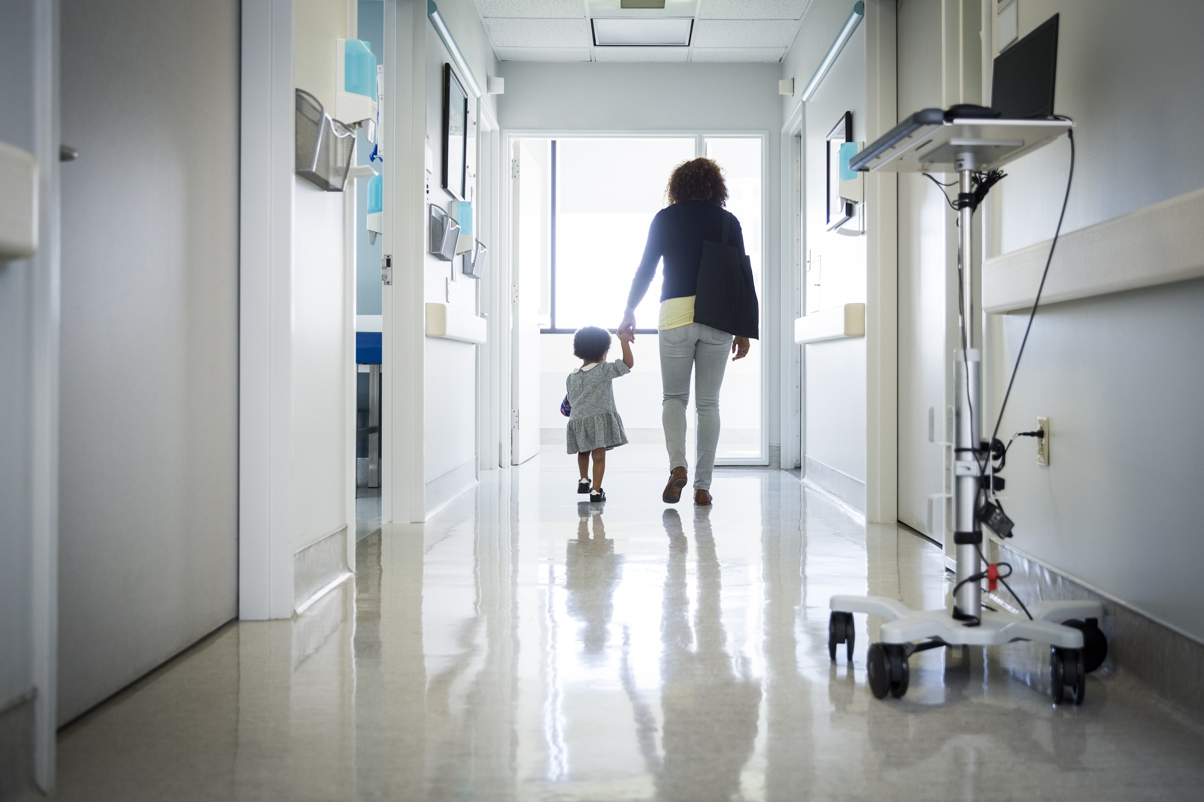 A woman and child walk hand in hand down a hospital corridor