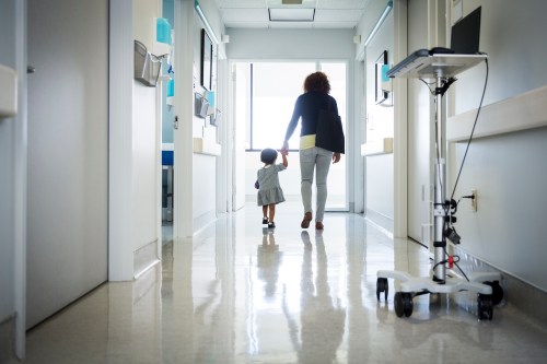 A woman and child walk hand in hand down a hospital corridor