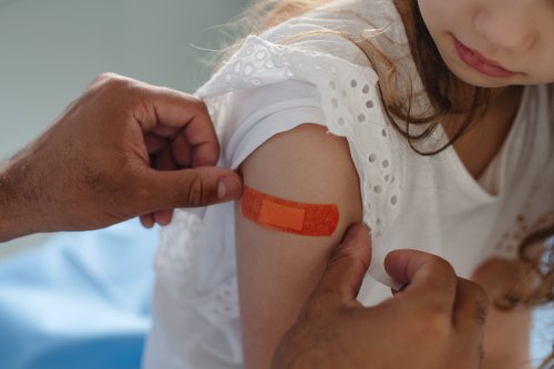 A doctor applies a bandage to a young girl's arm after she receives a vaccine.