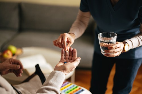 An anonymous female nurse giving pills and water to an unrecognizable senior in a home setting.