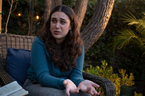 Mia Tretta speaks to someone out of frame to the left. The two are sitting outside.
