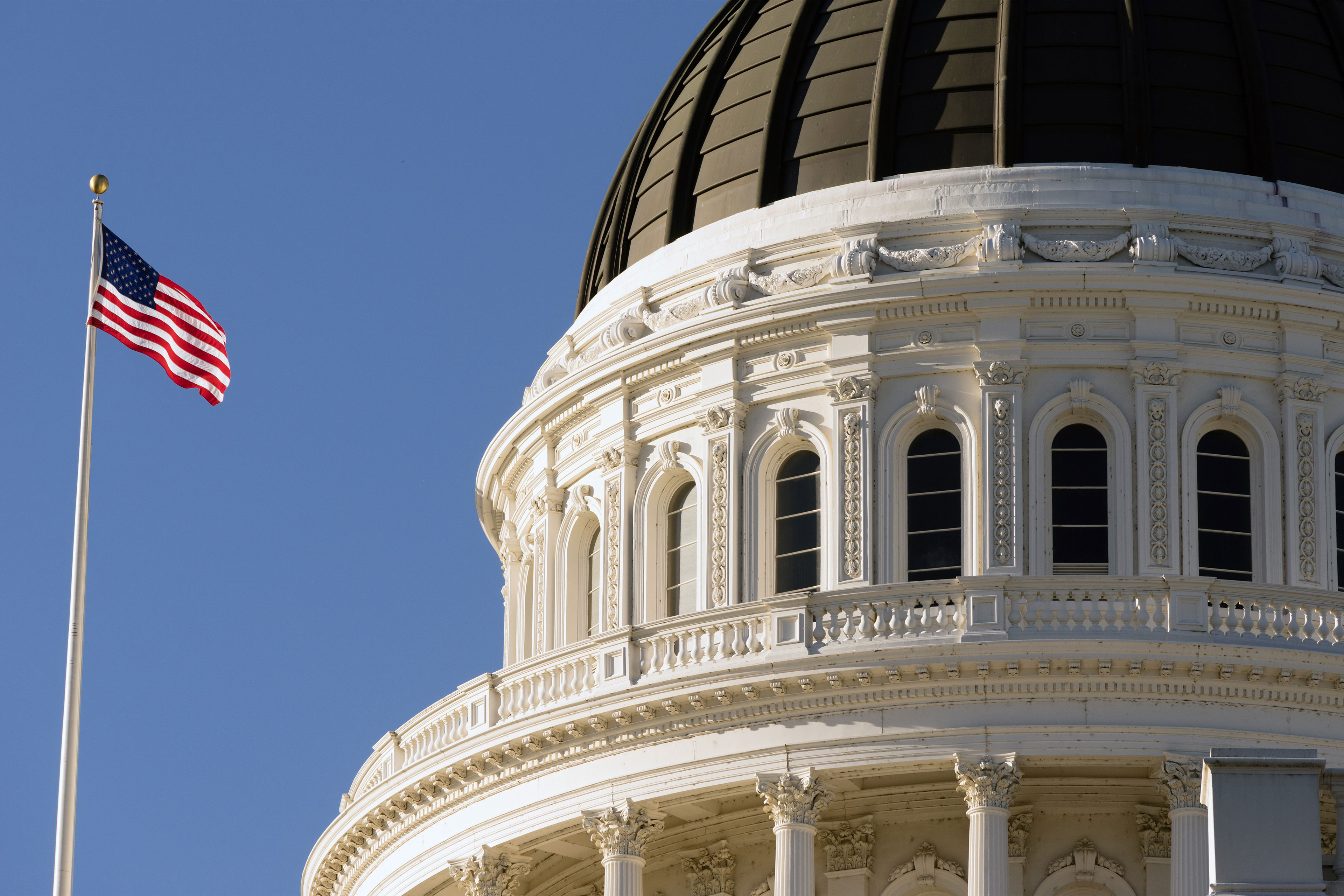 A close-up shot of the rotunda of the California Capitol in Sacramento. An American flag is seen on a pole to the left.