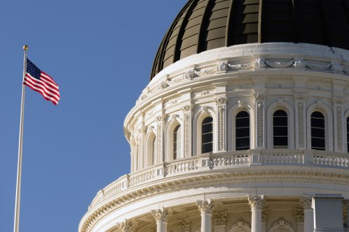 A close-up shot of the rotunda of the California Capitol in Sacramento. An American flag is seen on a pole to the left.