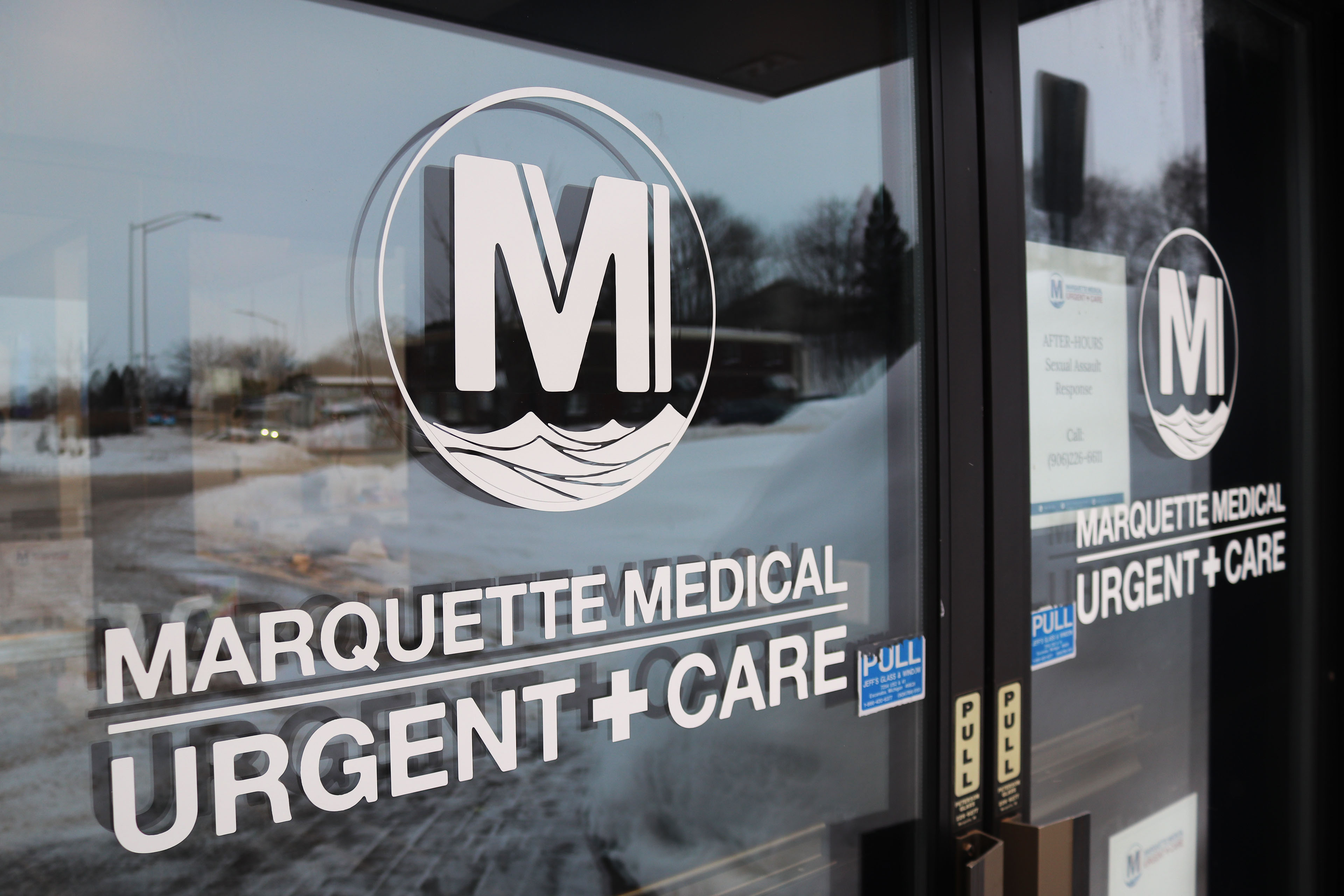 A close-up shot of a glass door at the entrance of Marquette Medical Urgent Care.
