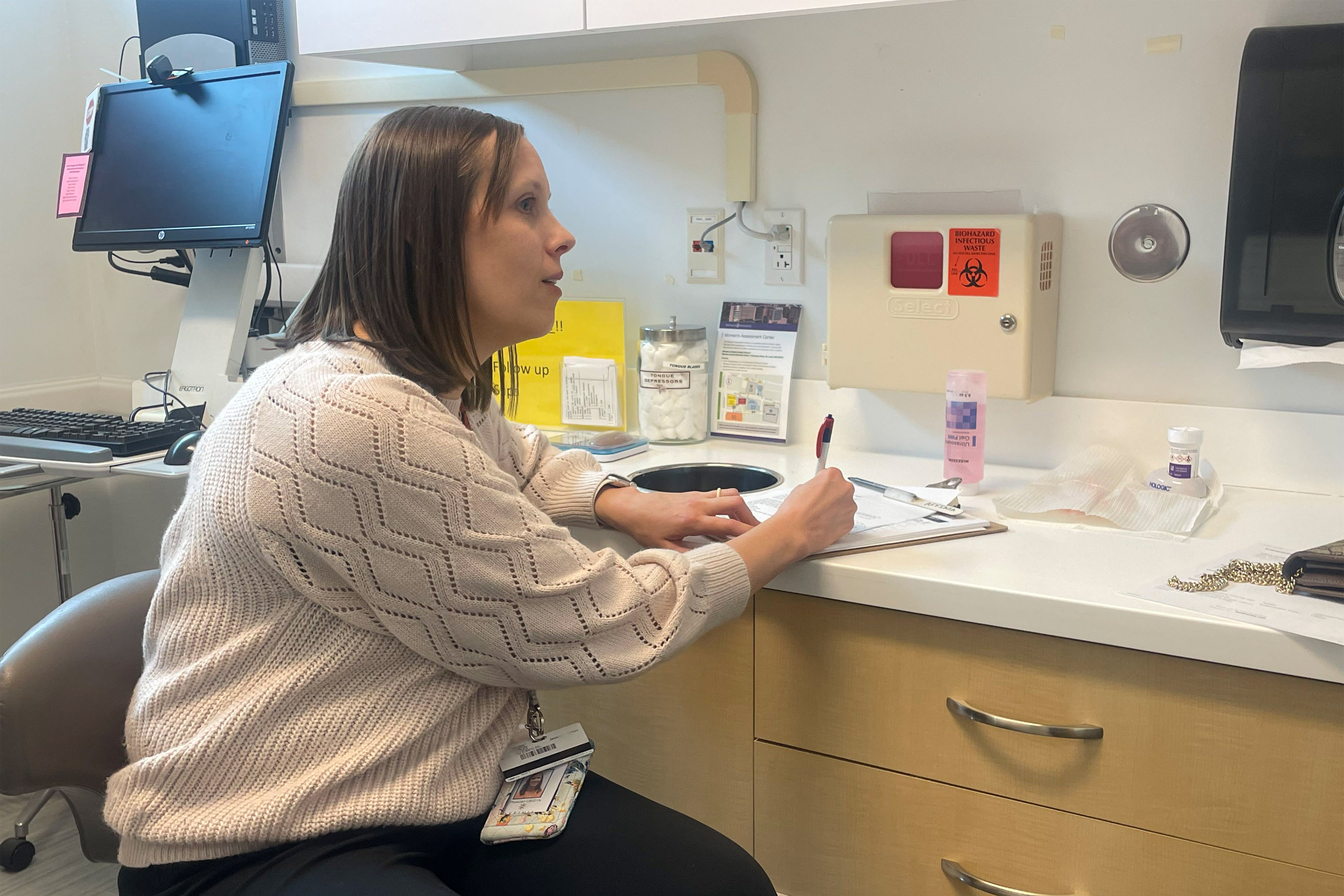 A doctor writes notes in an examination room while talking to a patient out of frame.
