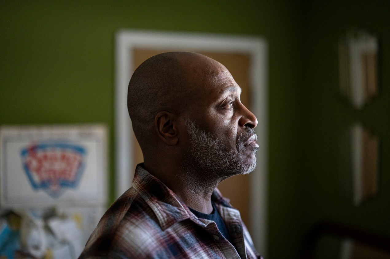 A photograph of the profile of a man, facing sunlight through a window, as he stands in a room with green painted walls